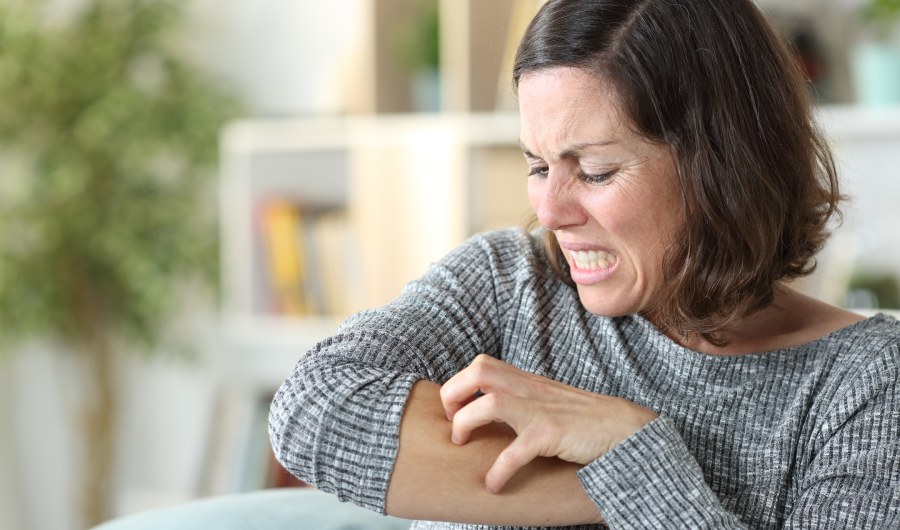 Middle age woman scratching itchy skin sitting on a couch at home